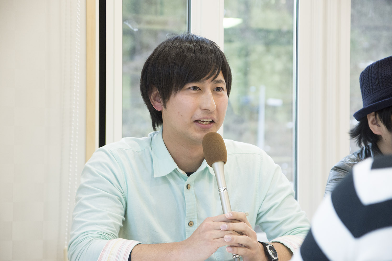 窓を背に座った原田さんが、マイクを持ってインタビューを受けている写真