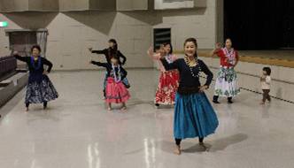 大人や子どもたちが右手を腰に当て、左手を横に伸ばしてフラダンスを踊っている様子を写した写真