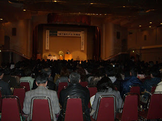 多くの人が集まる大きなホールで、ステージ上には演壇と花が飾られた国土政策フォーラムの様子を撮影した写真