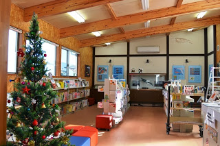 絵本や本棚が並んでいる室内にクリスマスツリーが飾られた図書館内の写真