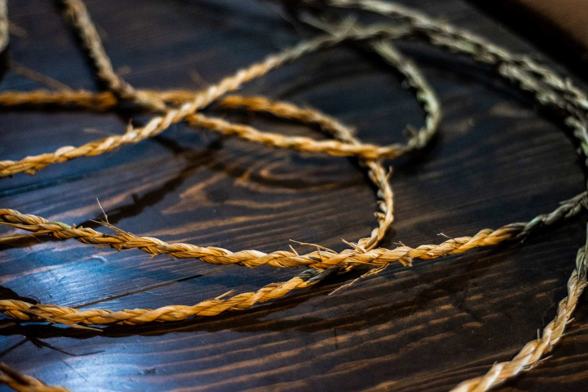 木製のテーブルの上に、複数の藁で編み込まれた縄が整然と並べられている写真