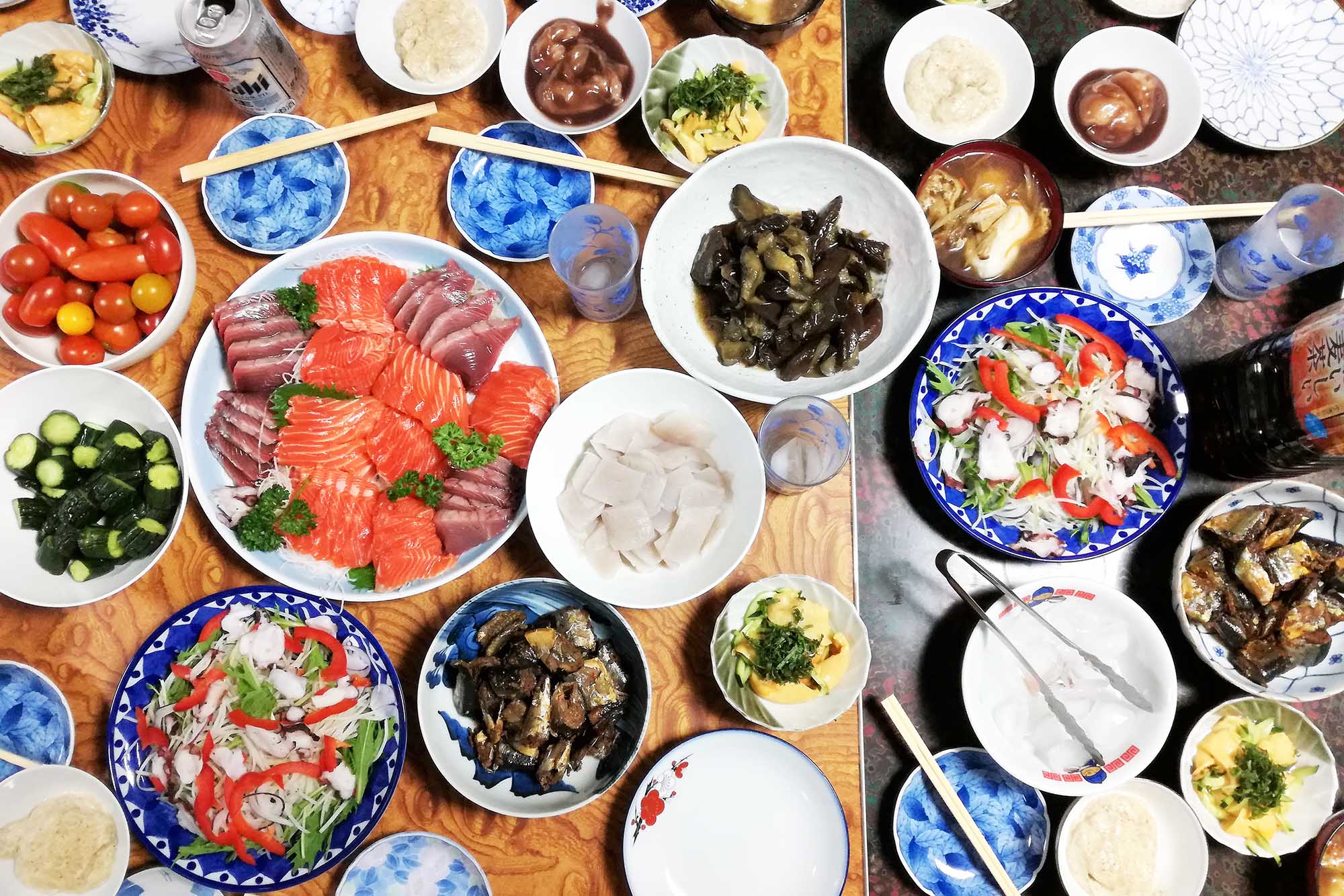 色とりどりの刺身や煮物、漬物、サラダなどがテーブルの上に所狭しと並べられ多数の豪華な料理が並んだテーブルの上を撮影した写真