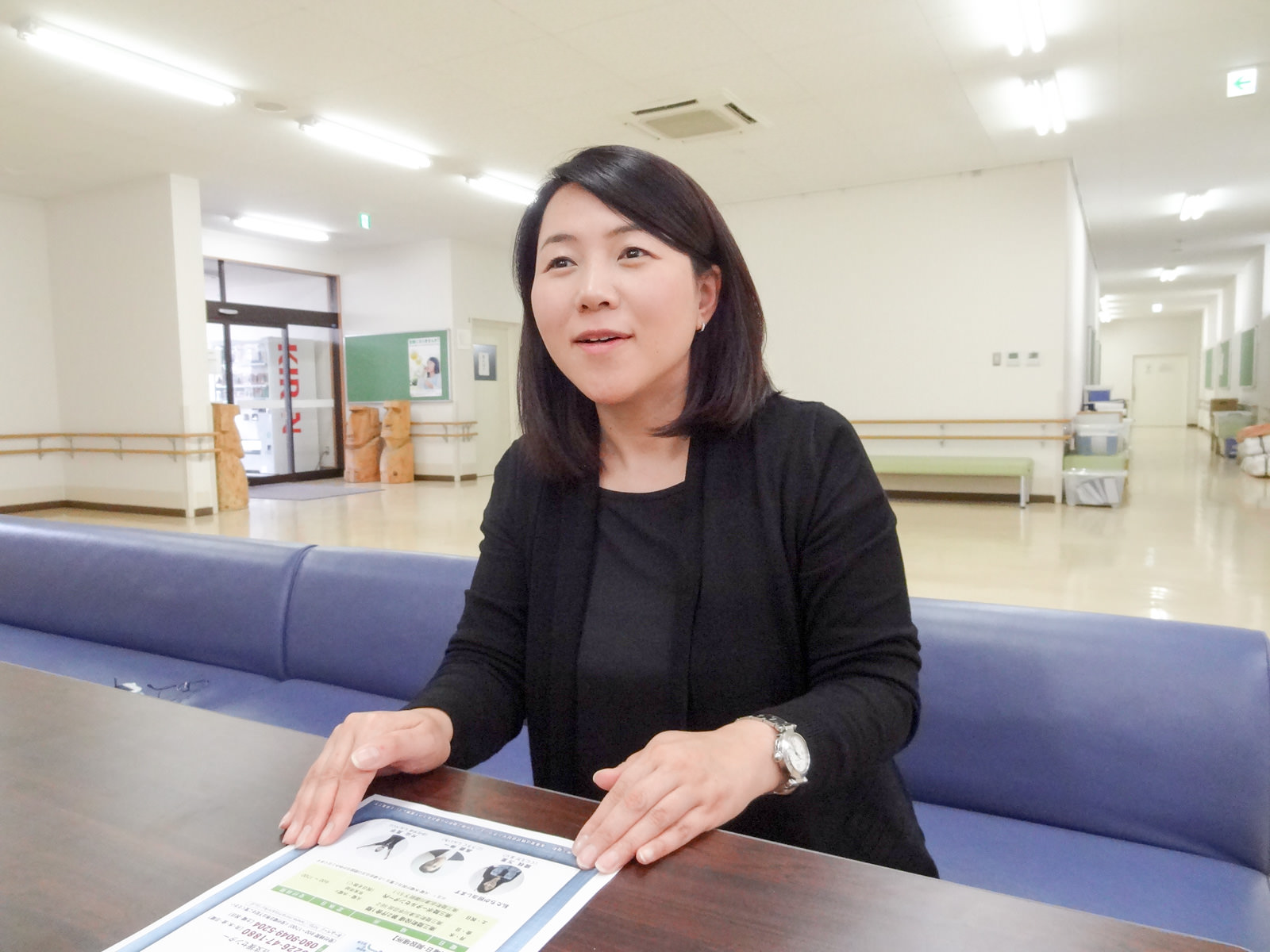 青いソファに座った國枝さんが、テーブルに置いた資料に手を置き、笑顔で話をしている写真