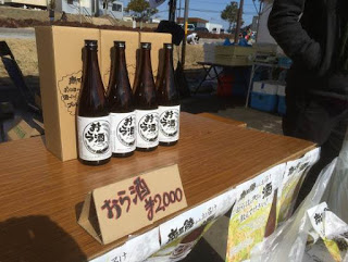 テーブルの上に白いラベルが貼られた茶色の酒瓶が4本並べて置かれ、その前に「おら酒 2000円」の札が立っている写真