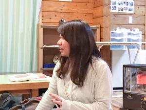 ストーブの近くで床に座り横を向いて話をしている渡邊佳菜さんの写真