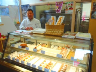 ガラスケースに並んだ様々な種類のお菓子が見え、店主の男性がカウンターの後ろに立って写っている写真