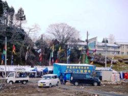 屋外のイベントエリアには複数のテントと車両があり、カラフルな旗がポールに掲げられているイベント会場の様子を写した写真