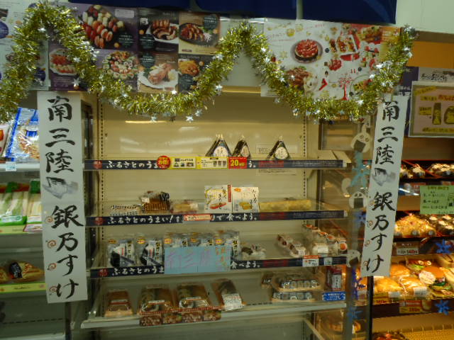 店内の、料理のポスターやキラキラしたモールが飾られたおにぎりの陳列棚の左右に、南三陸銀乃すけと書かれたポップが掲げられている写真