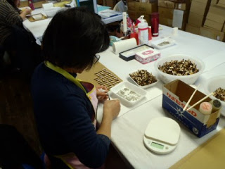 屋内の作業台で、女性が細かい部品を並べて作業をしている写真