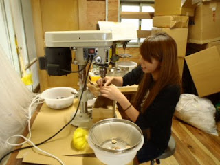 屋内の作業場で、女性が機械を操作している様子が写っている、作業中の写真