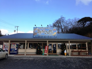 平屋建ての建物の屋根に「みなさん館」と書かれた大きな看板が掲げられた直売所の外観写真