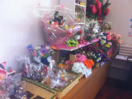 色とりどりの造花や花の形をした飾り物が棚やカゴの中に並べられ、ギフト用にラッピングされ並べられている写真
