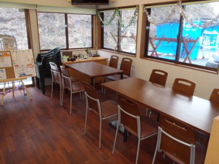 木目調のフローリングに茶色のテーブルと椅子が整然と並び、大きな窓から外の風景が見える飲食スペースの写真