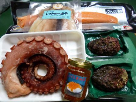 丸く巻かれたタコの足、瓶詰のいくら、真空パックされた魚など、さまざまな海産加工品が並べられている様子の写真