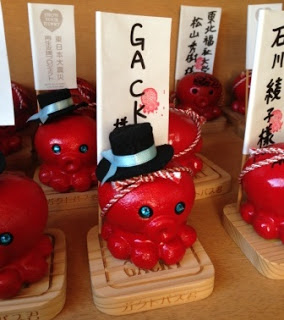 「Gackt様」の旗が台座に立てられ、水色のリボンがついている黒いシルクハットをかぶったガクトパス君の写真