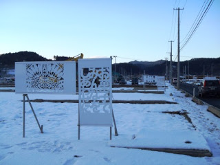 雪が積もった広い空き地に繊細な模様が切り抜かれた二つの白いきりこの看板が立っている写真