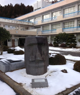 雪が積もった学校の前庭の一角にモアイの頭部が設置されている様子を写した写真