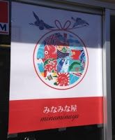 カラフルな海や魚のイラストが描かれた円形のデザインの下に「みなみな屋」と書かれたポスターが、ガラス戸に貼られている写真