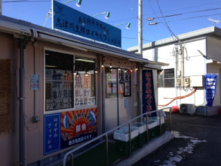 建物の上に青い看板があり、「ロイヤルフィッシュ」と書かれた看板も掲示されている生鮮ロイヤルフィッシュさんの店舗の外観写真