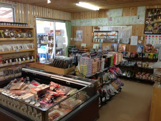 陳列棚や冷蔵ケースに、お菓子、飲み物、調味料など様々な商品が並んでいるマルアラ及川商店の店内を写した写真