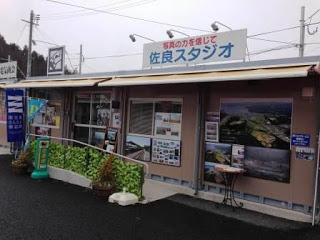 仮設商店街の一角にあるプレハブ造りの建物で、「佐良スタジオ」と書かれた看板の下に写真展示があり、震災記録を伝える佐良スタジオの外観写真