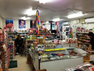 店内の陳列棚にはたくさんの商品が並び、中央には冷蔵ケースが置かれ店員が座っているマルタケ大衆ストアの店内の写真