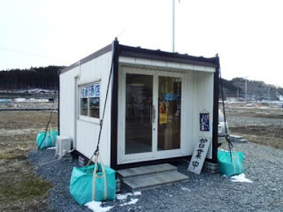 広々とした場所にあるプレハブの仮設店舗で、入り口に営業中と書かれた看板が立てかけられている佐藤酒店の外観写真