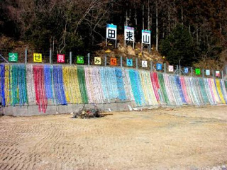 上部には「田束山」の看板、その下に「全世界のみなさんありがとう」と色とりどりの背景に一文字ずつ書かれた看板があり、その下に簾のように折り鶴が連なって飾られている写真