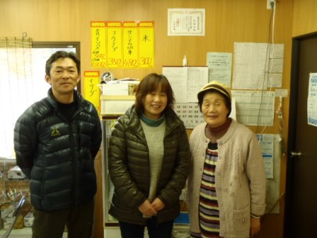 たくさんの掲示物が貼られた壁の前に左から隆明さん、美紀さん、かつ子さんが3人横に並んで笑顔で写っている写真