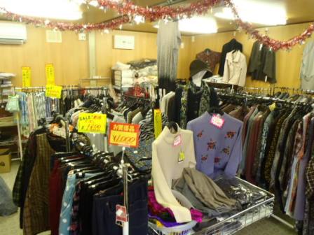 多数の上着やスカートなどの衣類がハンガーや壁に掛けられ、モールで天井が華やかに飾りつけされた店内の様子を写した写真