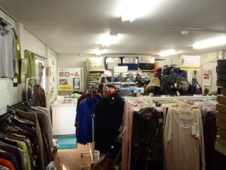 店内には色とりどりの衣類がハンガーや棚に掛けられていて、奥には木製のカウンターと商品が並んでいるマルエーさんの店内の写真