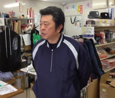 紺色のジャージを着た店主の山内義申さんが、店舗内で手を後ろで組んで写っている写真