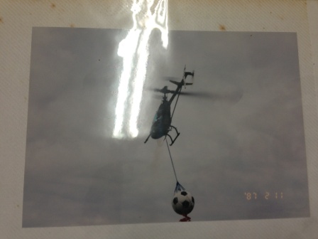 リモコン操作の小型ヘリコプターがサッカーボールをロープで吊り下げて空中を飛行しながら運んでいる様子を捉えた写真
