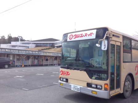 バスの前面に「ウジエスーパー」と書かれたベージュ色の移動販売車のバスが駐車場に停まっていている写真