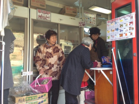 バスの出入り口付近にあるレジ台で、年配の女性が精算をしており、買い物かごを持った客の女性がレジに並んでいる様子の写真