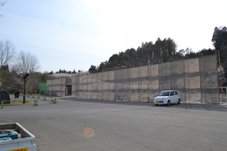 白い軽自動車が舗装された駐車場に停まり、その奥には工事中の仮囲いがある写真