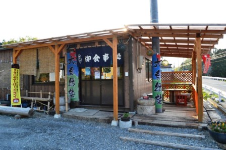 「御食事処」と書かれたのれんが店先にかけられ、右側にはひさしのついた屋外の休憩スペースも設けられている「津の宮 大自然塾」の外観写真