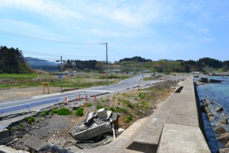 右側には海が広がり、そのすぐそばにコンクリートの堤防があり、堤防の脇には壊れたコンクリートが見られる写真