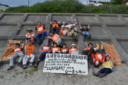 コンクリートの防波堤の斜面にオレンジのビブス着たボランティアの方がが座り、「長須賀海水浴場清掃大作戦」と書かれた横断幕を持っている集合写真