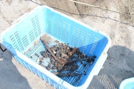 青いプラスチック製のかごの中に、釘や木片、石やガラス片などのがれきが入っている写真