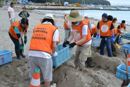 2人で青いかごをを持ち、かごを使って砂をふるいにかけてがれきを取り除く作業をしている様子を写した写真