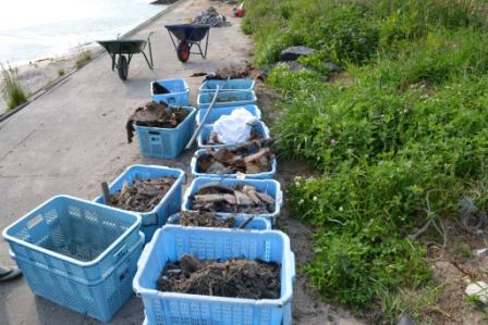ビーチのコンクリートの通路に青いプラスチック製のかごが並べられ、清掃活動で出た異物がかごいっぱいに入っている様子の写真