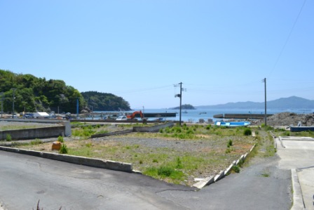 空き地が広がり港では土が山のよう積まれ重機による工事の様子の写真