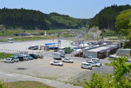 大きな空き地に自動車やトラックが整理され並べられ奥には仮設住宅が並んでいる三島神社から撮影した写真