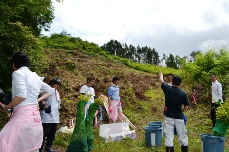 人々が丘の斜面の前に集まり、作業の指示を受けている様子の写真