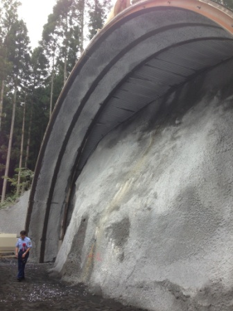 トンネルの坑口のそばに男性が立っており、巨大な岩盤になっている掘削直前のトンネル入口の写真