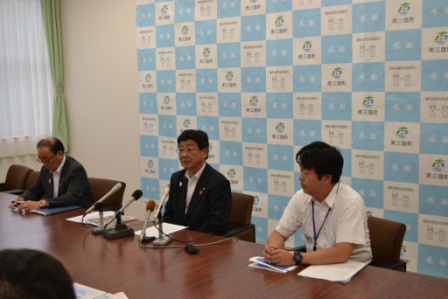 佐藤町長と関係者の3人の男性がテーブルに着席し、佐藤町長がマイクを通して話をしている様子の写真