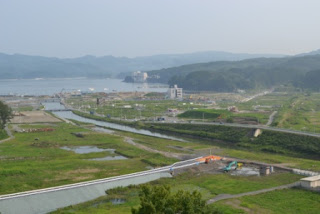 緑豊かな田園が広がる中央には穏やかに流れる川があり、その奥には連なる山々と青く広がる海が見える、自然の美しさが詰まった風景の写真