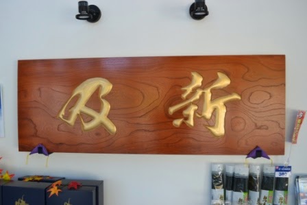 木目のある茶色い板に金色で「及新」と立体的に彫られた看板が店内に飾られている写真