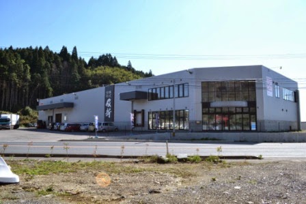 山に囲まれた場所に工場が併設された白い外壁の株式会社 及新の建物が立っている写真